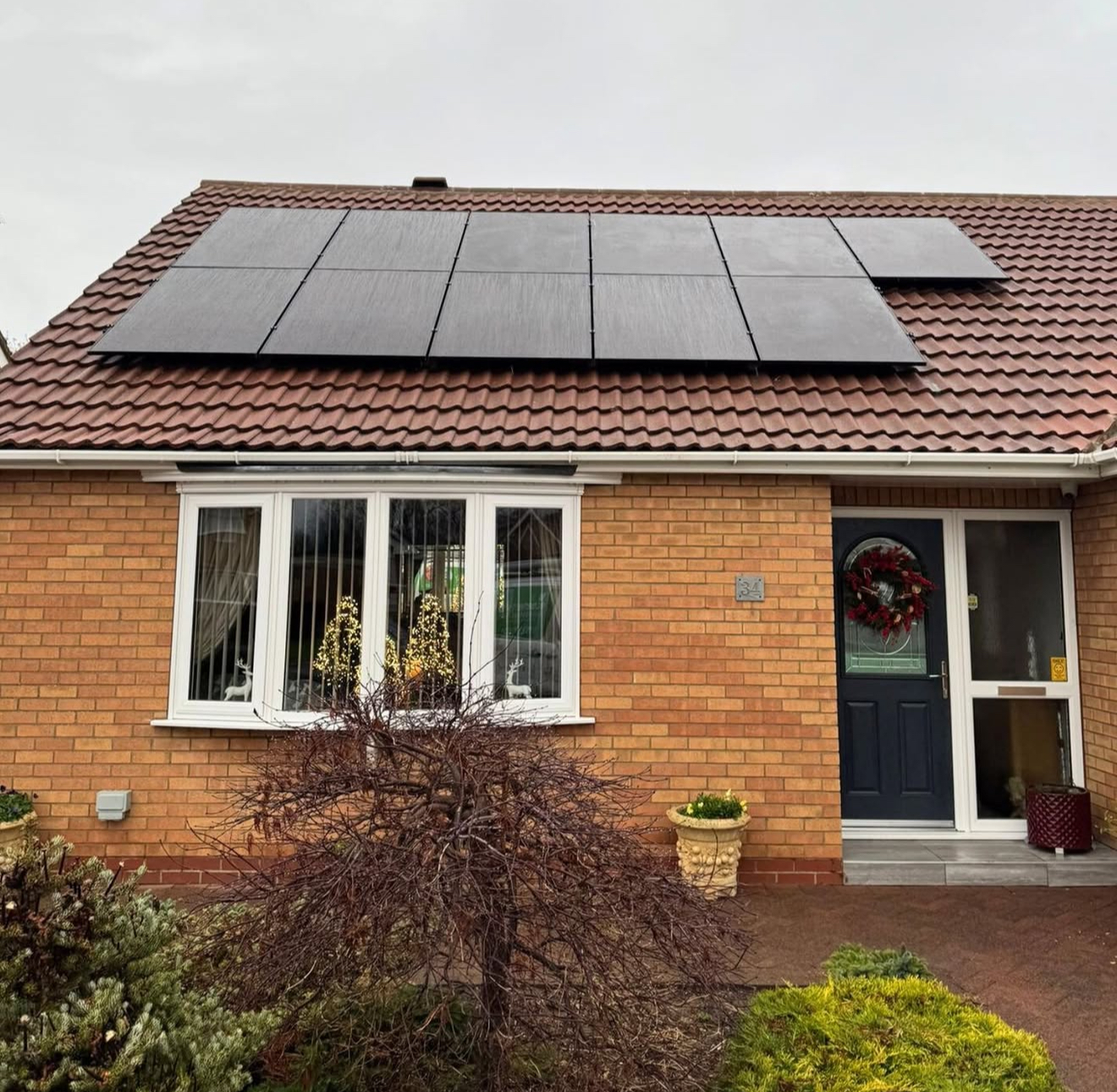 Black solar panels on the tiled roof of a brick bungalow